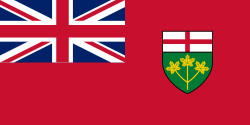 A red flag with a large Union Jack in the upper-left corner and a shield in the centre-right
